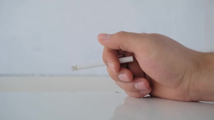 一名男子手持香烟在白色木桌和白色背景的闪亮表面。