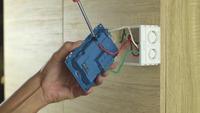 电工正在使用螺丝刀卸下木墙上电气插头的电线。