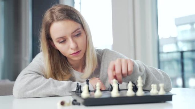 肖像年轻迷人的女人玩国际象棋游戏在线使用笔记本电脑在厨房的餐桌上。