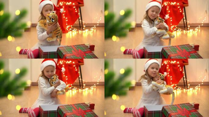 快乐的小女孩打开礼品盒，在圣诞树旁边拿出玩具老虎
