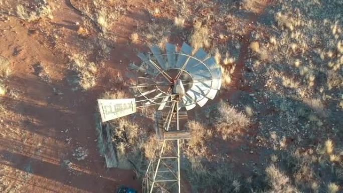 太阳在半干旱的风景相机上击中风车的缓慢转动的金属叶片，俯视风车到地面航拍视频