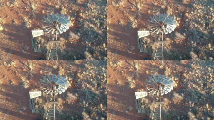 太阳在半干旱的风景相机上击中风车的缓慢转动的金属叶片，俯视风车到地面航拍视频