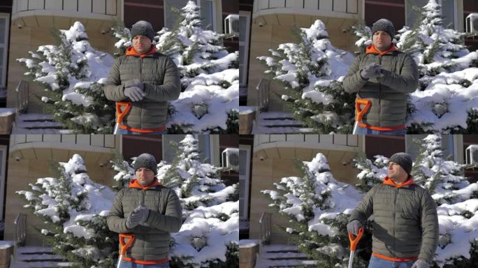 在一个阳光明媚的日子里，一个男人在公寓的院子里用铲子除雪。那家伙用铁锹手动从街上铲起白雪。冬季工作和