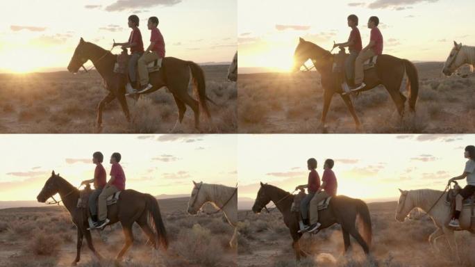 慢动作少年美国原住民纳瓦霍男孩和女孩在戏剧性的日落下在亚利桑那州纪念碑谷或犹他州附近的戏剧性沙漠中骑