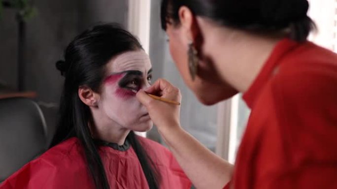 女化妆师在为万圣节之夜化妆时，使用眼影在客户的脸上制造虚假的血液动机