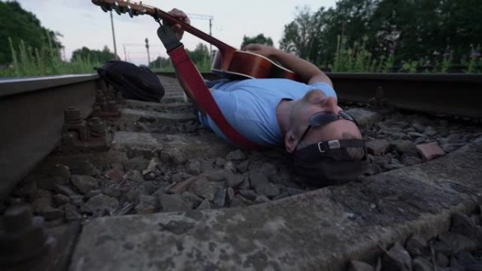 戴着墨镜的胡须的男性音乐家躺在铁路的卧铺上