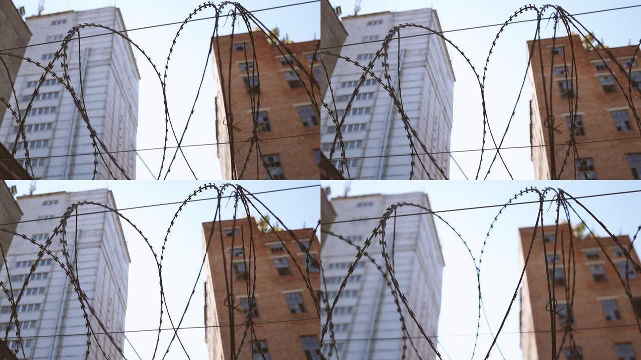 高高的混凝土围栏，铁丝网映衬蓝天背景。窗户破碎的废弃砖砌建筑