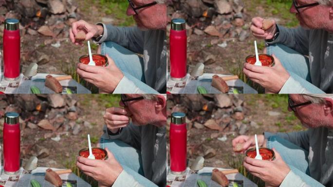 一个有食欲的人用叉子吃番茄酱罐头鱼。户外野餐
