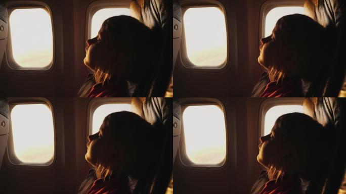 在任何地方和任何位置睡觉，一个小女孩正在飞机上的扶手椅上睡觉，晨光穿透飞机窗户