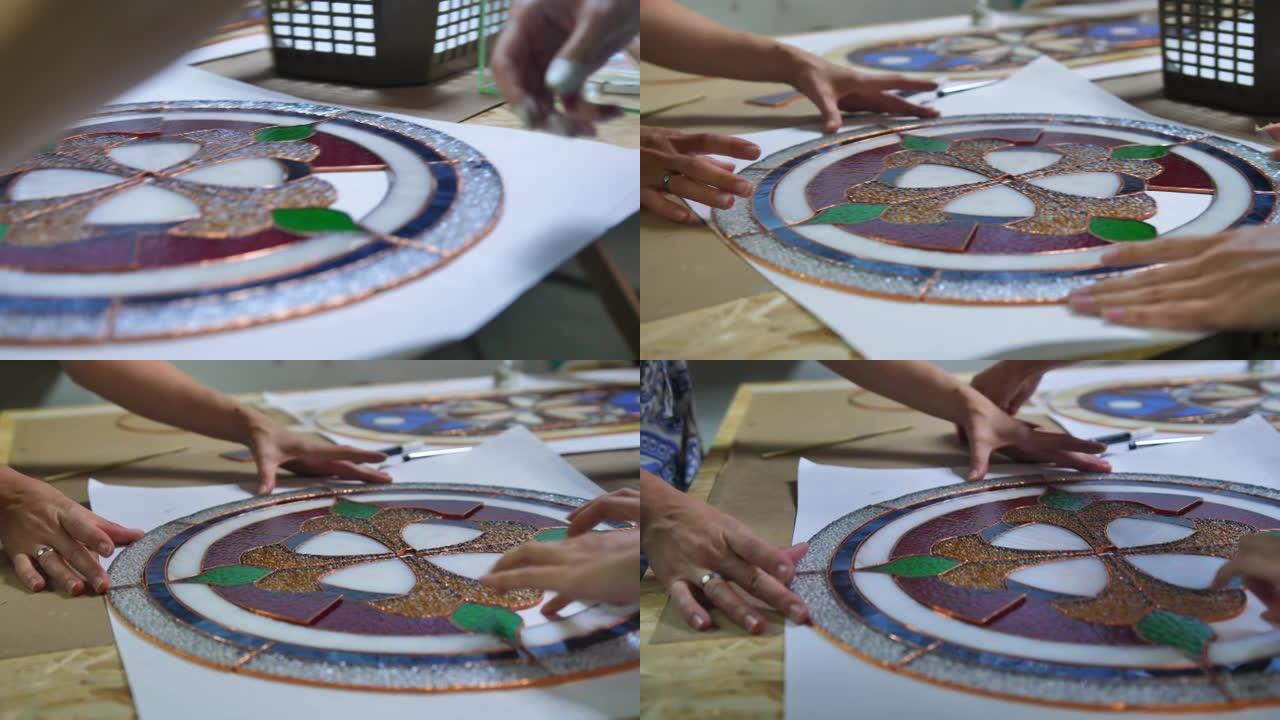 两位艺术家用彩色玻璃窗组装作品。两个女人的手。工艺品，工艺品。蒂芙尼彩色玻璃。图片详情