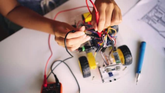 用万用表读取带有传感器的自动驾驶机器人汽车原型的电压的女机器人工程师的手