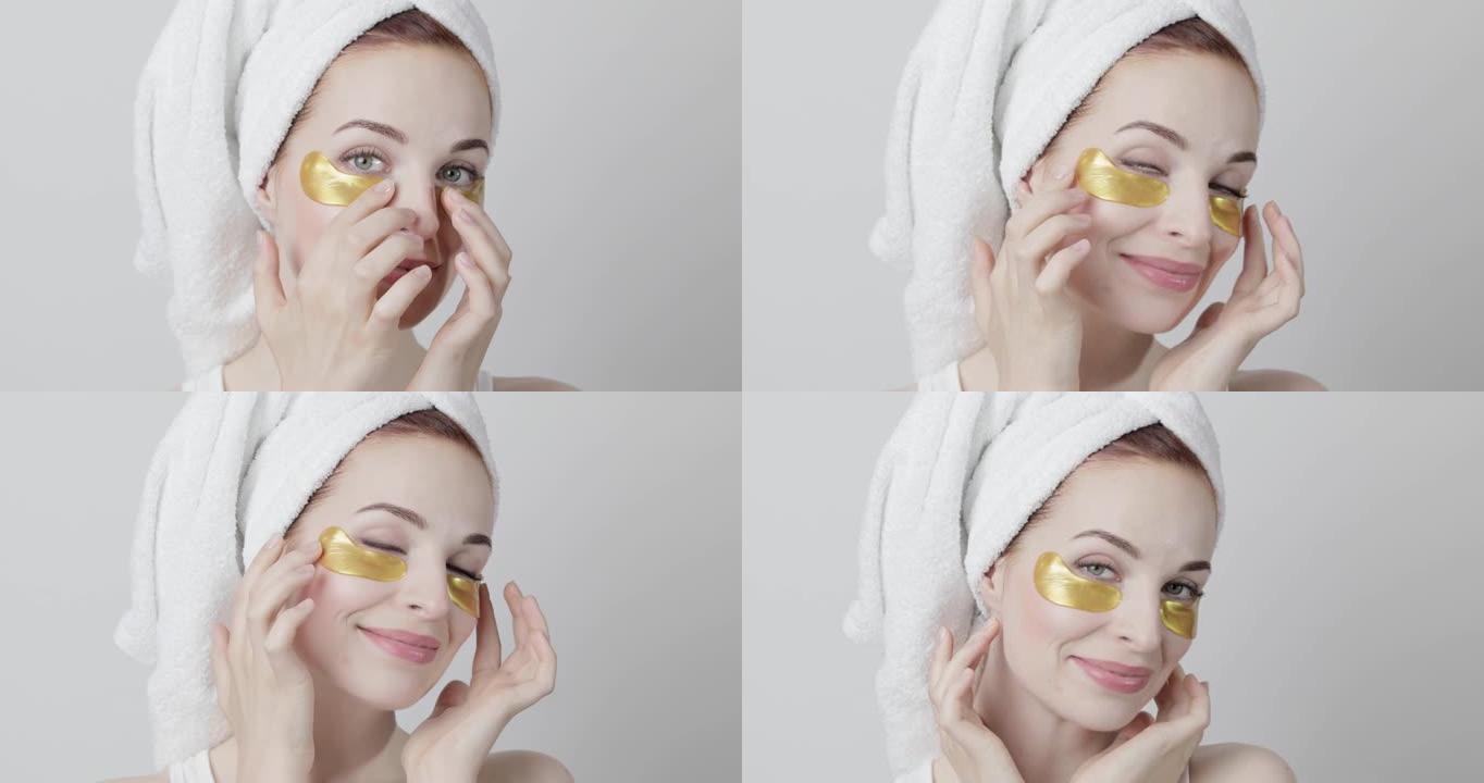 美丽微笑的女人头上的毛巾，在家庭水疗过程中应用金色的眼罩