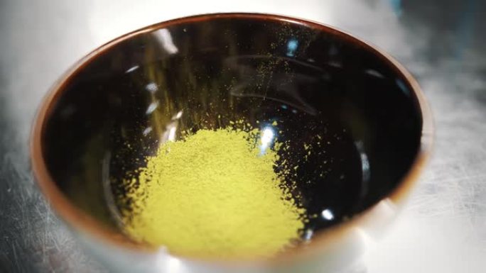 抹茶。特写。在一个黑色的小碗中过筛绿色抹茶茶粉。制作日式抹茶绿茶