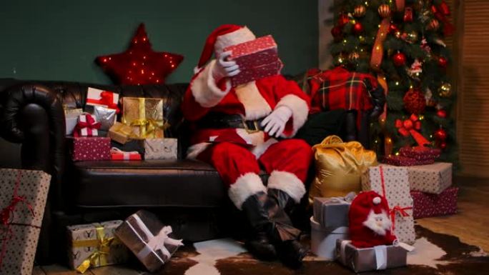 圣诞老人读信，并把礼物放在袋子里送给孩子们。穿着红色西装戴着帽子的胡子的老人坐在装饰房间里的沙发上，