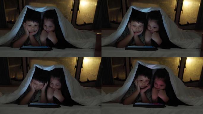 亚洲兄弟姐妹在大篷车的毯子下使用平板电脑。当他们晚上躺在前面时。房车假日旅行
