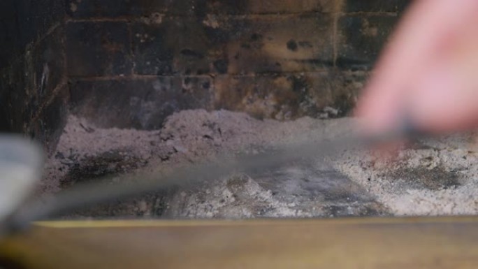 一个人用旧的铁簸箕搅拌，并在木柴燃烧后从木柴中收集灰烬和煤渣，并将其关闭。使用后清洁壁炉