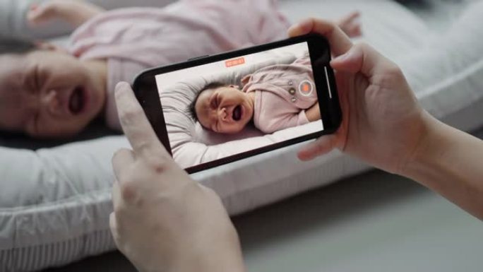 妈妈用手机按下录制躺在靠垫上的可爱的婴儿视频。