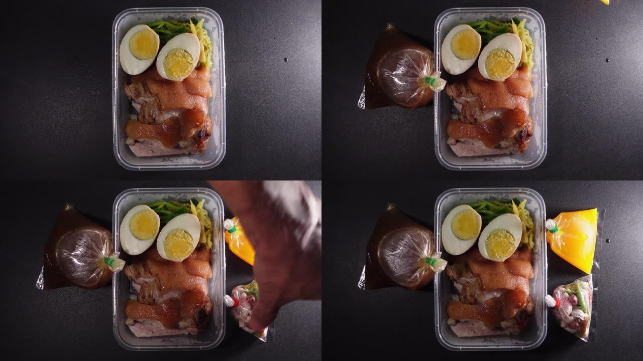 猪腿饭装在一个塑料盒中，上面放着蘸酱。黑桌上的肉汤和大蒜辣椒粉，泰国菜