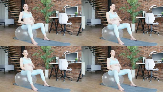 孕妇坐在家里的健身球上拍肚子