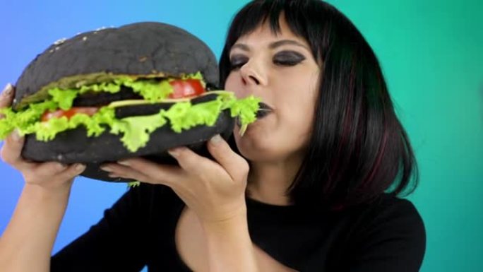 女人在聚会上吃一个大的黑色汉堡。