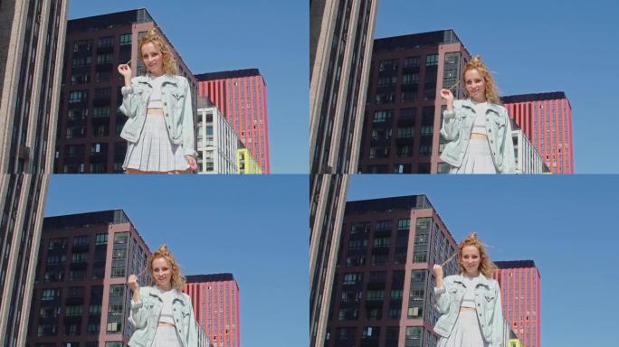 穿着牛仔夹克的快乐女孩在屋顶上抚摸她的卷发，欣赏城市的景色。阳光明媚的日子里，神秘的金姜女人在露台上
