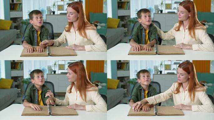 盲人男孩坐在家里的女老师旁边学习阅读盲文书，孩子的手指在一张纸上移动