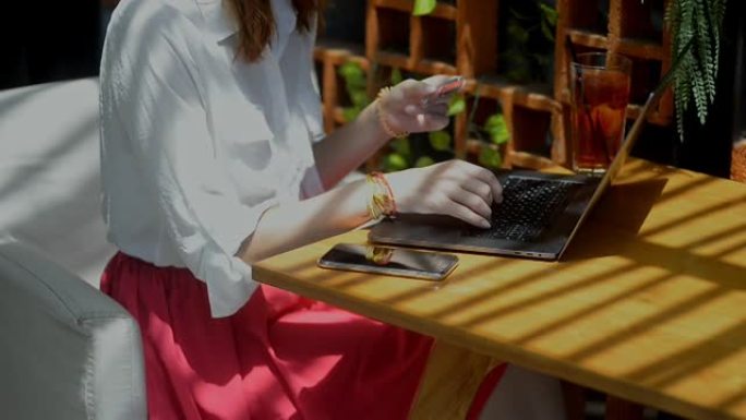 年轻女子在夏季露台的办公桌上使用笔记本电脑和信用卡在线购物