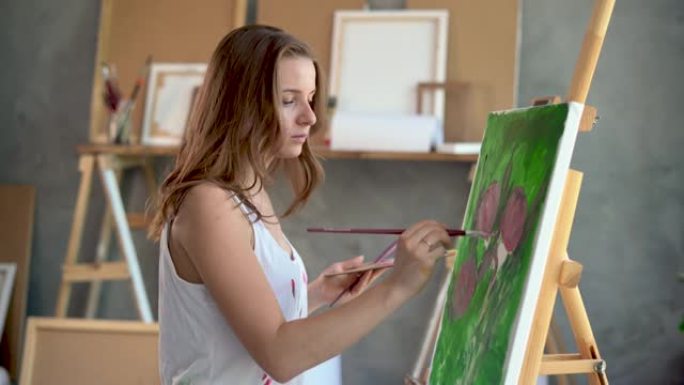 一位女艺术家的特写肖像她用画笔和画布上的丙烯酸颜料用牡丹画了一幅画。工作室里到处都是乐器。