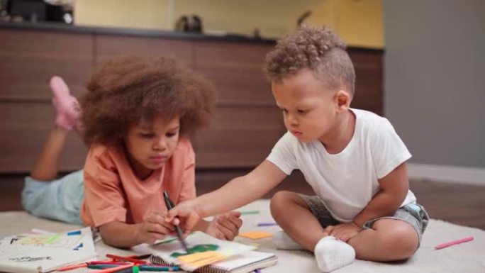 两个可爱的混血儿孩子躺在家里的地板上，用记事本的铅笔画画。富有创造力的跨种族兄弟姐妹，小女孩和蹒跚学