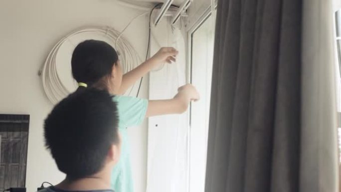 亚洲女孩帮助母亲在家里的窗户附近悬挂新的白色窗帘，检疫生活方式理念。
