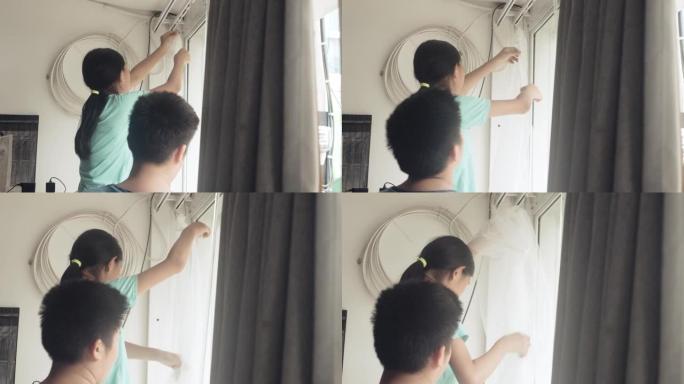 亚洲女孩帮助母亲在家里的窗户附近悬挂新的白色窗帘，检疫生活方式理念。