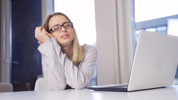 年轻的金发女人戴着眼镜在笔记本电脑上工作，伸展运动超负荷。计算机专业的女学生