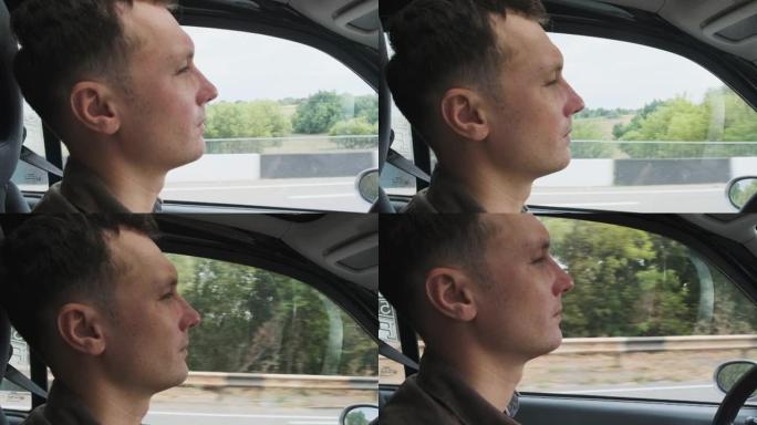 特写镜头中年轻人的肖像，晴天在高速公路上开车。背景绿树。慢动作4k镜头