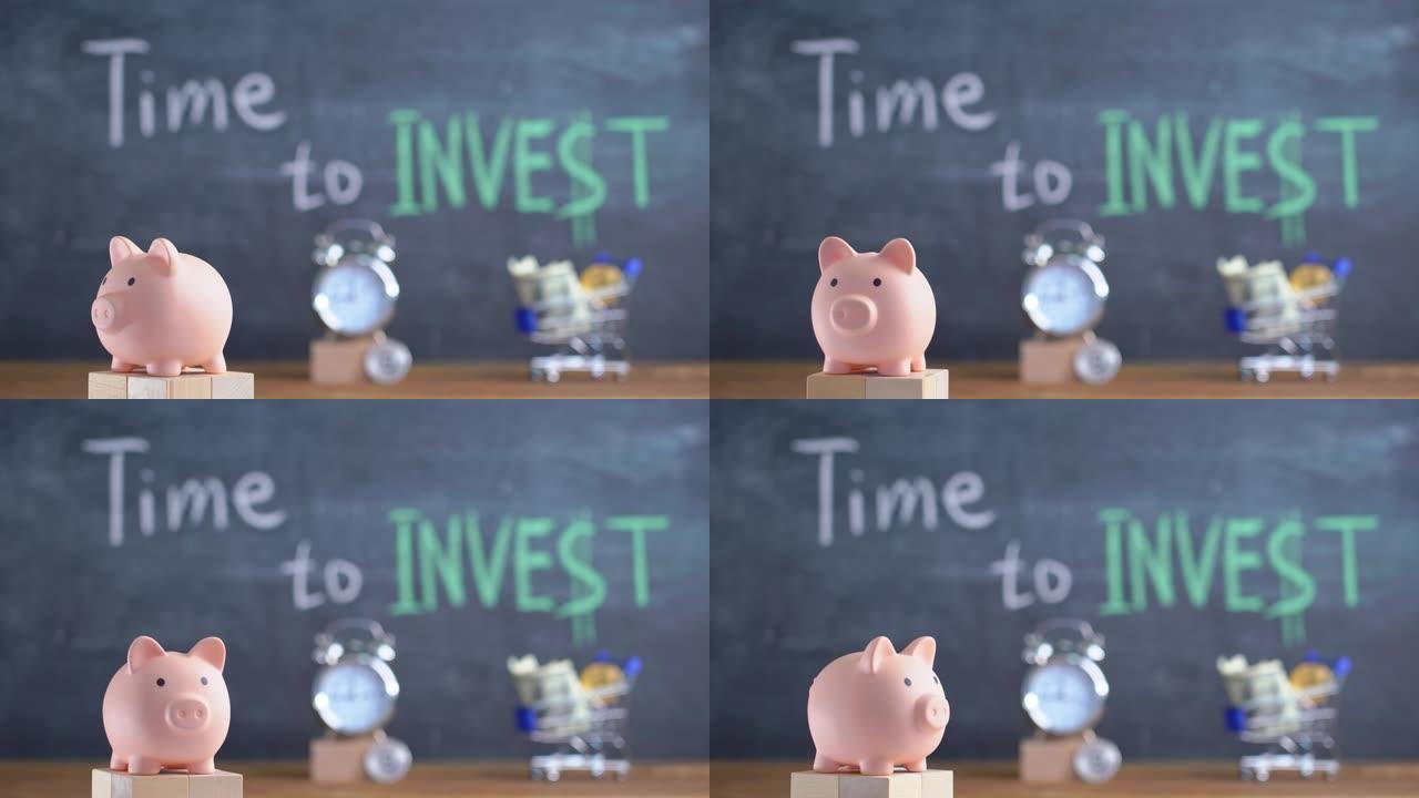 是时候投资概念了。在黑板的背景上旋转粉红色的存钱罐，上面写着 “投资的时间”