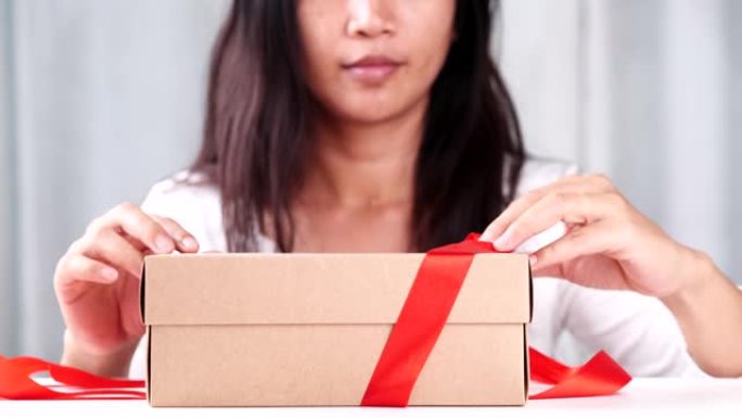 女人手打开乡村礼品盒在家里赠送红丝带蝴蝶结领带。捐赠的概念季节，圣诞节，新年快乐，生日，情人节，周年