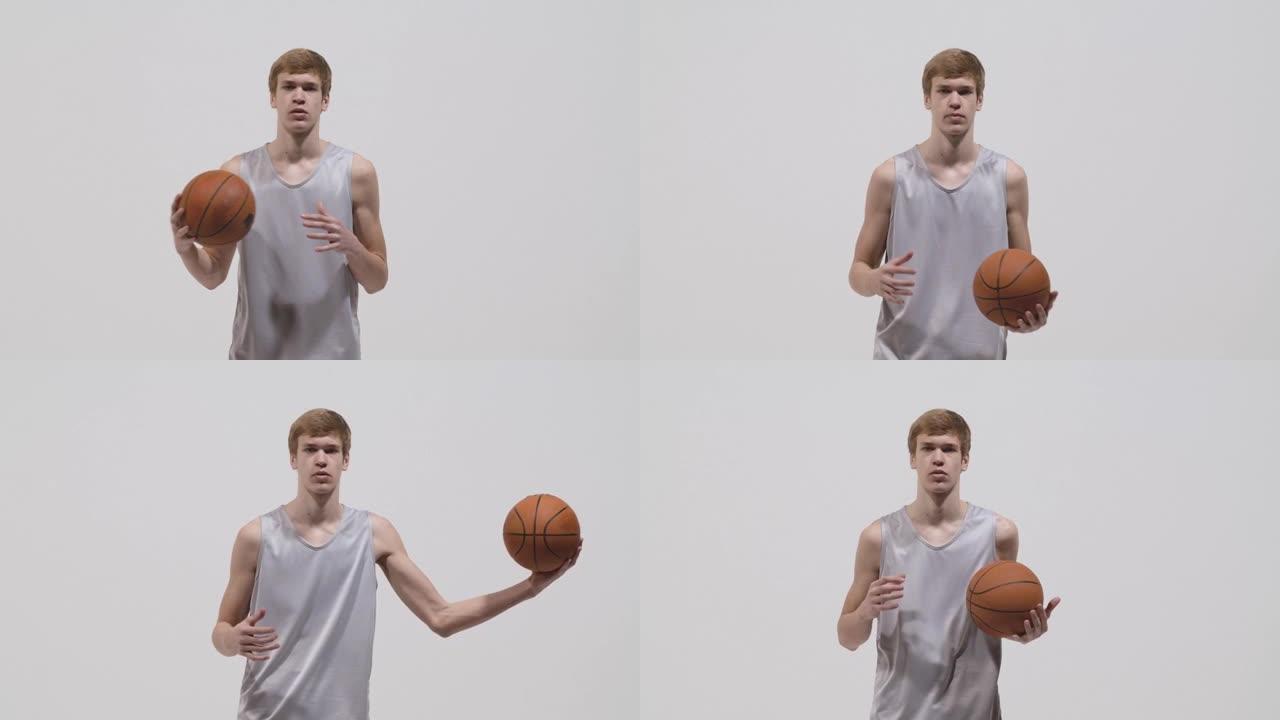 年轻篮球运动员看着相机，手把手扔球的肖像。穿着运动服的运动员在白色工作室背景下摆姿势。特写。慢动作准