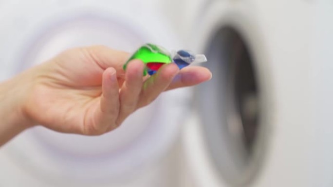 一个女人拿着洗衣机用洗衣粉的胶囊。