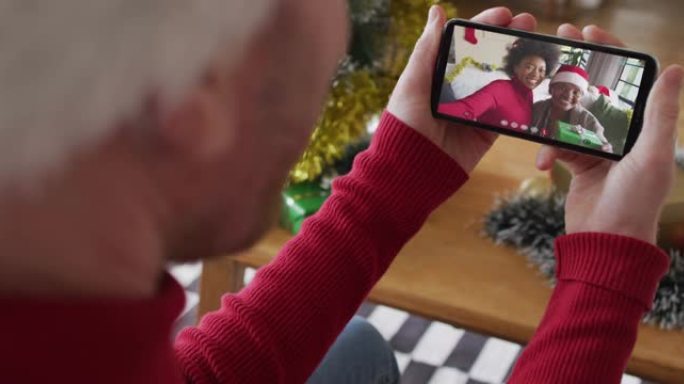 白人男子使用智能手机进行圣诞节视频通话，屏幕上有微笑的家人