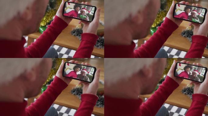 白人男子使用智能手机进行圣诞节视频通话，屏幕上有微笑的家人