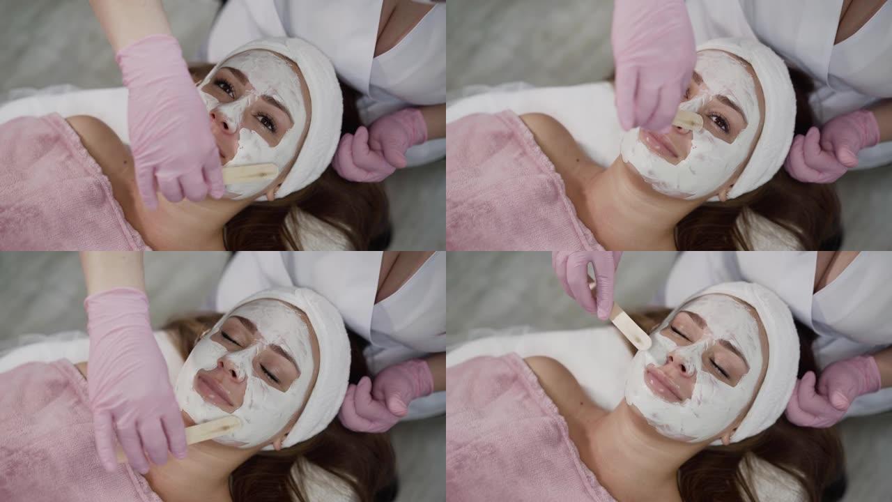 美容院在女性脸上涂抹抹刀粘土面膜的水疗程序