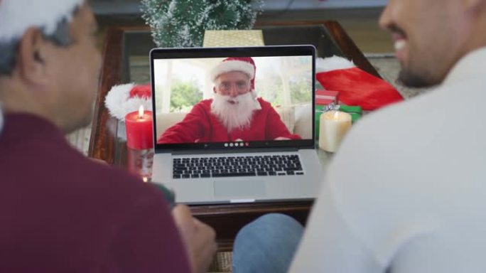微笑的混血儿父子使用笔记本电脑与圣诞老人在屏幕上进行圣诞节视频通话