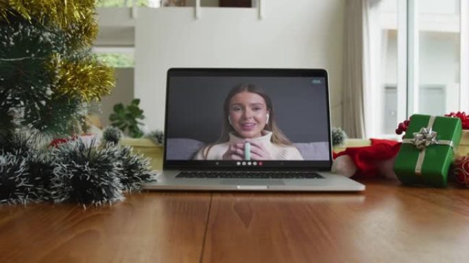 微笑的白人妇女在笔记本电脑上的圣诞节视频通话中喝咖啡