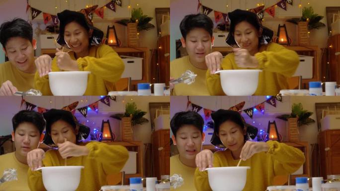 亚洲女孩戴着女巫的帽子，晚上和哥哥一起在家做糖霜饼干，万圣节的生活理念。