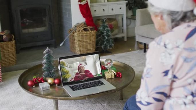 高级白种人妇女挥手和使用笔记本电脑与屏幕上的女人的圣诞视频通话