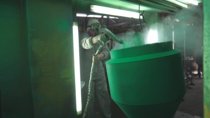 工厂室内的工业喷漆工艺。油漆工在特殊的展位上喷涂绿色油漆。安全磨损技术人员在生产中工作。专业车间的油