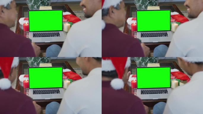 微笑的混血儿父亲和戴着圣诞老人帽子的儿子在绿色屏幕上进行笔记本电脑圣诞节视频通话