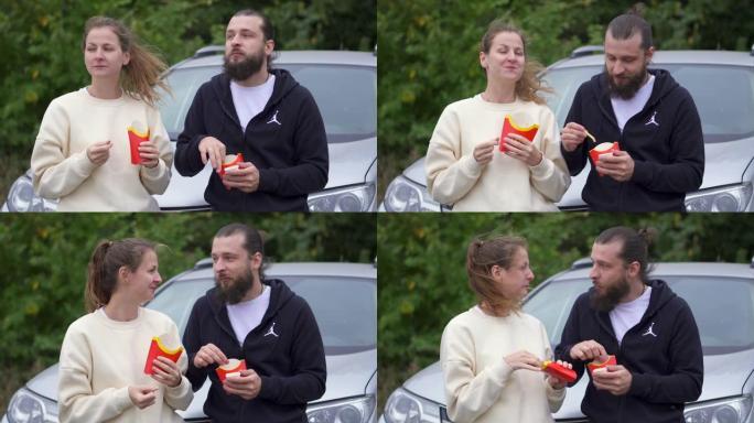 一对夫妇在公园约会时一起吃麦当劳薯条。垃圾食品浪漫小吃。森林里的绿树。青少年在车上吃零食。说笑。快乐