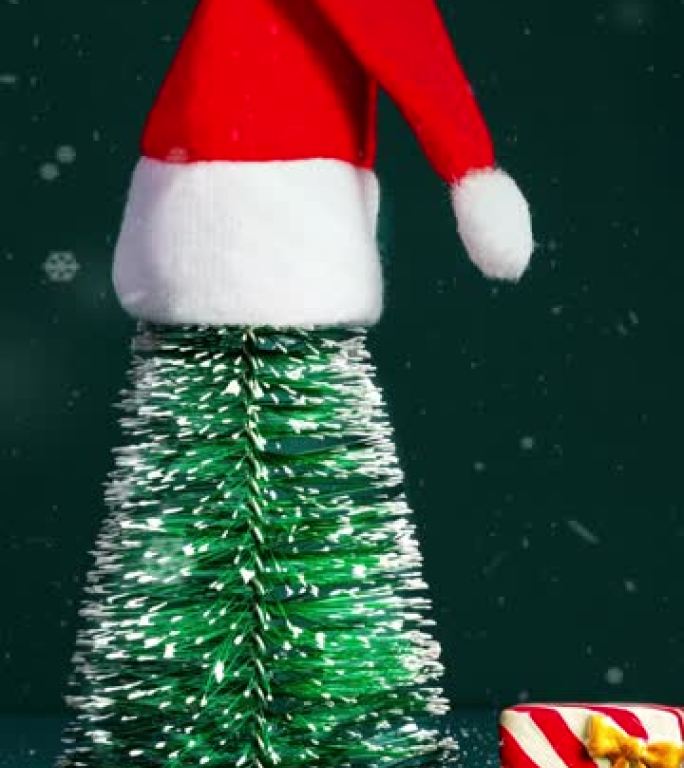 垂直圣诞快乐和新年快乐下雪，绿色松树上戴着埃德圣诞老人帽子，深绿色背景上戴着礼品盒。节日庆祝贺卡