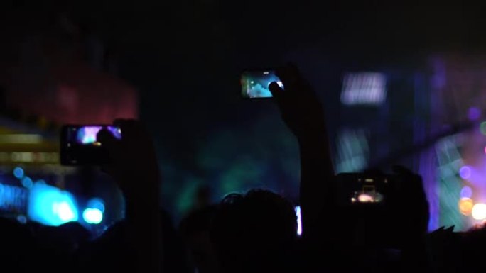 人群中的抽象剪影，举起手来，跳舞，拿着智能手机。不在焦点阶段。手持视频