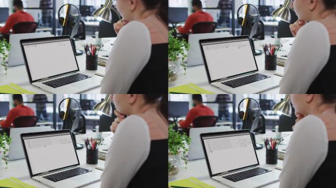 白人妇女坐在办公桌前观看笔记本电脑屏幕上的编码数据处理